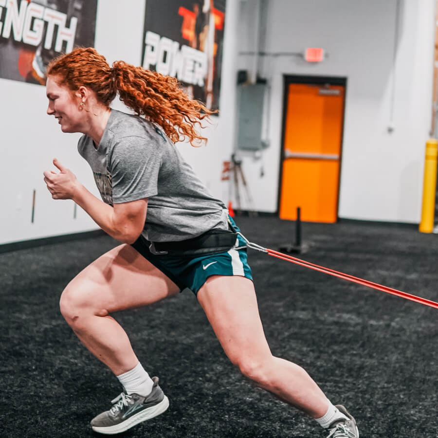 A girl in a gray shirt runs with a rope tied to her waist