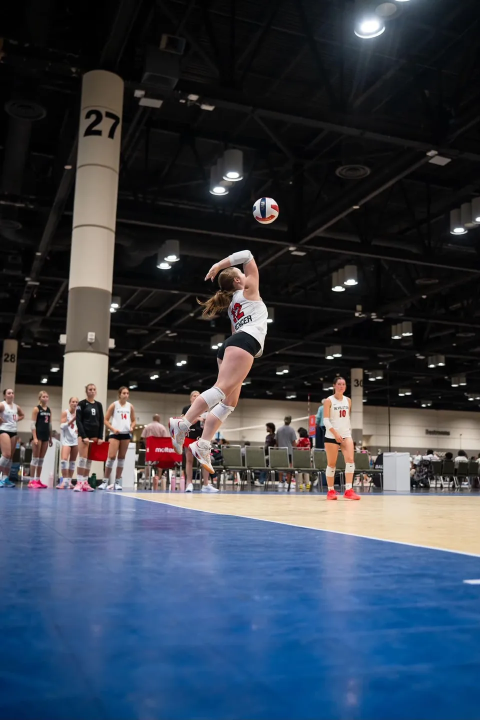 Kylie Spencer leaping to serve during an indoor volleyball match